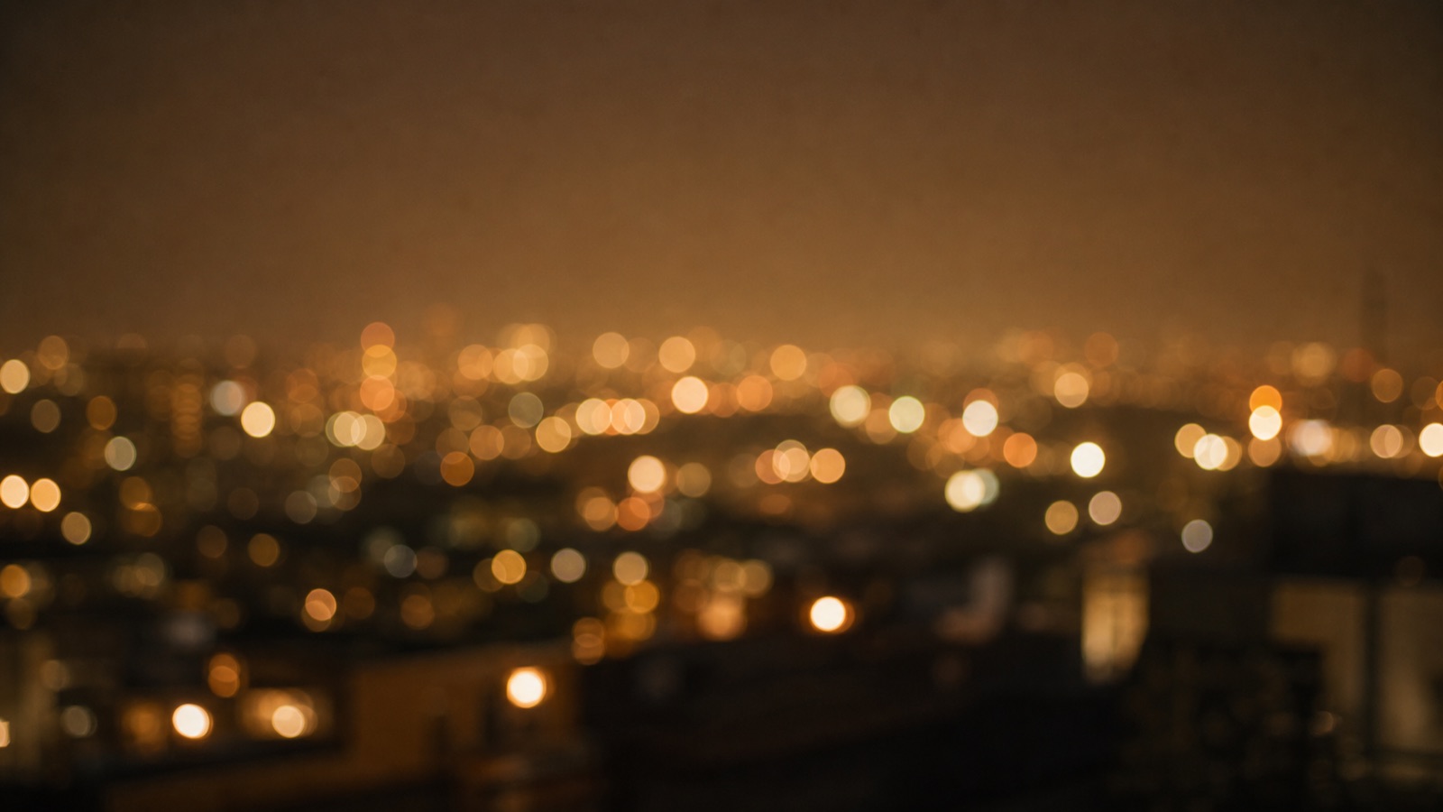 แสงไฟเมืองยามค่ำเบลอเป็นวง bokeh มองจากดาดฟ้า โทนอำพันและทอง